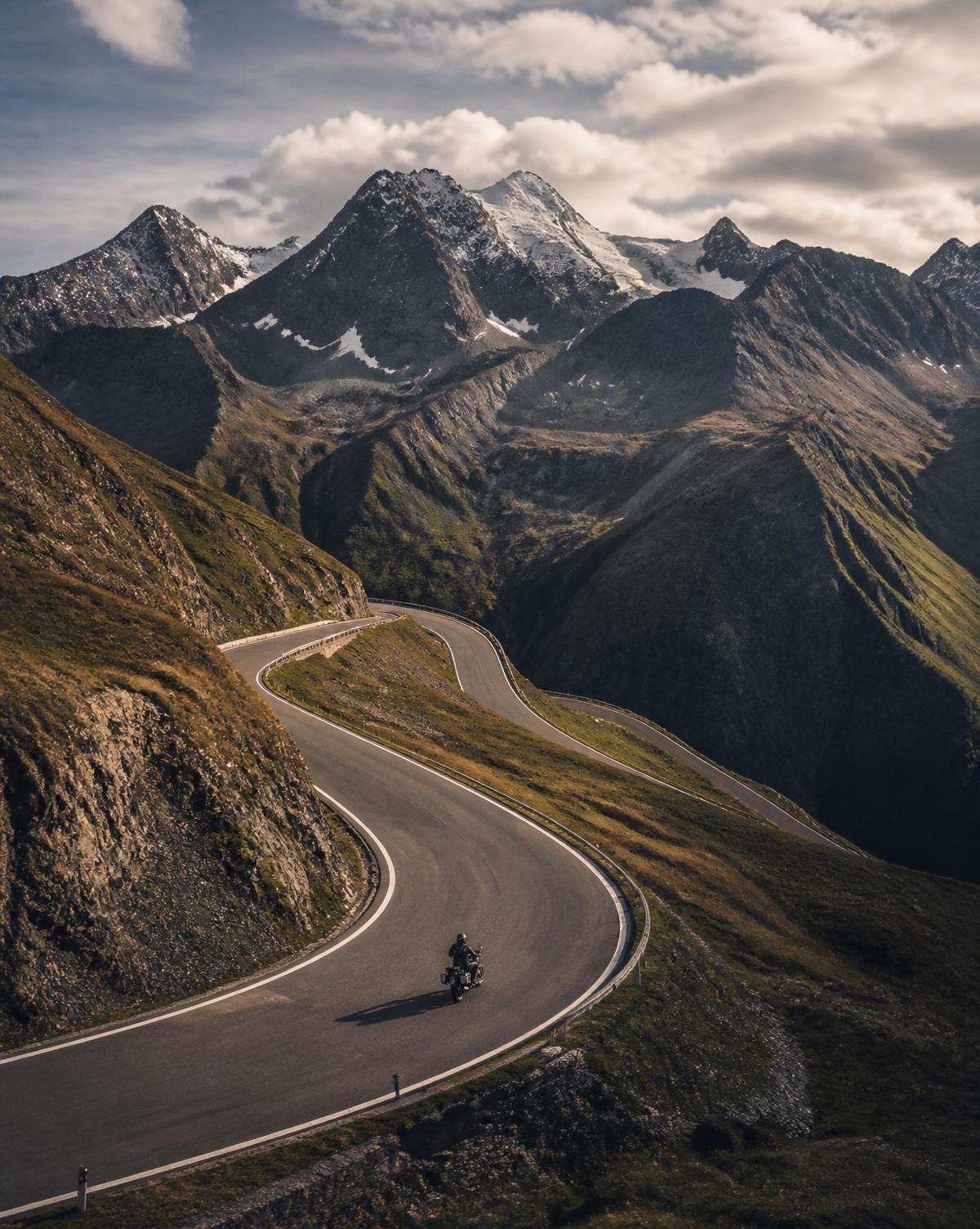 Kurvige Alpenstraße mit einem Motorrad vor Bergpanorama